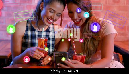 Image of media icons over happy caucasian female friends with drinks Stock Photo
