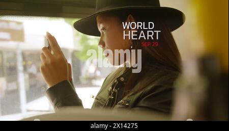 World heart day text banner against asian woman wearing a hat using smartphone in the bus Stock Photo
