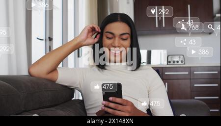 Image of social media icons and numbers over biracial woman using smartphone Stock Photo
