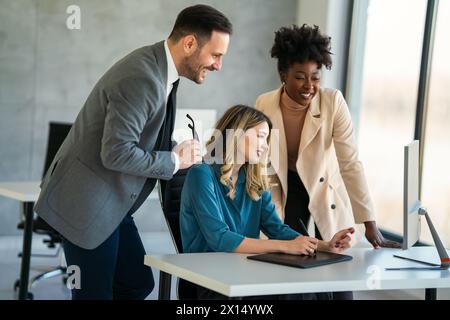 Group of happy multiethnic business people in formal wear gathered around computer in office Stock Photo