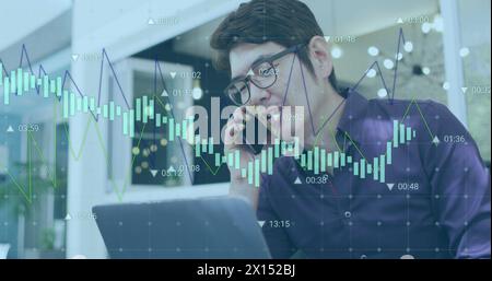 Image of graphs with changing numbers, asian man working on laptop and talking on cellphone Stock Photo