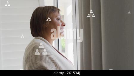 Image of profile icon flowcharts over senior thoughtful caucasian woman looking through window Stock Photo
