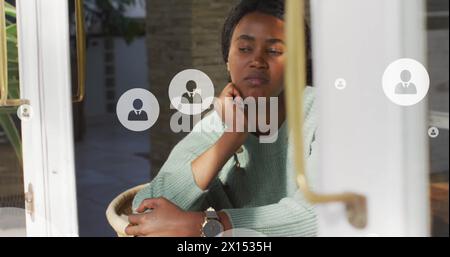 Image of profile icon in circles over thoughtful african american woman looking through window Stock Photo
