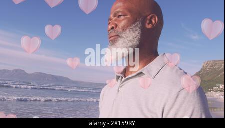 Image of hearts over senior african american man at beach Stock Photo