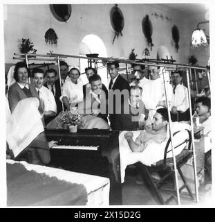 CHRISTMAS AT 104 BRITISH GENERAL HOSPITAL : OBSERVER STORY - Ward singing - left to right:- Nursing Officer M. Hawkins of Acomb, Hexham, Northumberland (seated at piano back to camera) Nursing Officer A. Ramage of Fforestfach, Swansea Pte. J. Johnstone of 12 Dewsbury Place, Longsight, Manchester VAD Iseult Passy of St.Anta, Carris Bay, Cornwall L/Cpl. F. Mayo of 20 Newhall Street, Walsall, Staffs Mountaineer T. Summers of Campbell, 183 Bolton Street, Glasgow, C.4. Pte. N. Webster of 85 Greaves Street, Little Hordon, Bradford, Yorks British Army Stock Photo