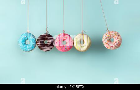 Newton's cradle from doughnuts. Collision balls made from donuts. Harm of sugar, donuts time or healthy diet concept. Dependence on flavoring, diabetes problems, weight loss. Stock Photo