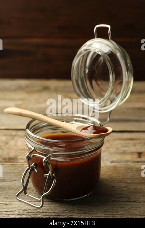 Tasty barbeque sauce in jar and spoon on wooden table Stock Photo