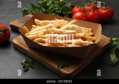 Tasty potato fries, cheese sauce in paper container and products on black table, closeup Stock Photo