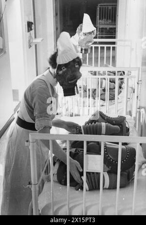 GAS DRILL AT A LONDON HOSPITAL: GAS MASKS FOR BABIES ARE TESTED, ENGLAND, 1940 - Two nurses each pump the bellows of a baby gas respirator in order to supply the child wearing the mask with air, during a gas drill at a London hospital, 1940 Stock Photo