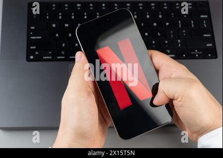 New York, USA - April 6, 2024: Popular Netflix mobile app on smartphone screen in hands on laptop keyboard background Stock Photo
