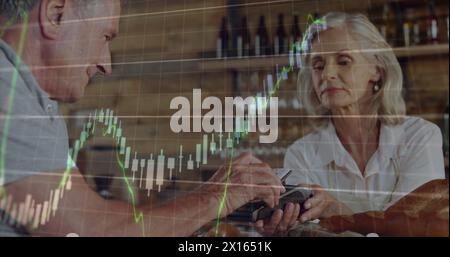 Image of multiple graphs over caucasian senior man tapping credit card on reader held by woman Stock Photo