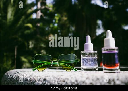 Tropical summer cosmetics. Cosmetic serum, oil extracts against lush greenery of tropics. Skin care products. Beauty nature. Heart-shaped sunglasses. Stock Photo