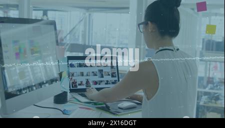 Image of graph and changing numbers over asian woman working over laptop and desktop Stock Photo