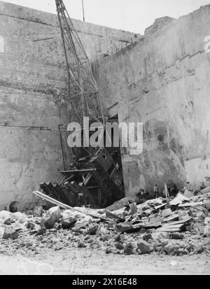BOMB DAMAGE IN MALTA AFTER BIGGEST RAID YET. 7 APRIL 1942. BOMB DAMAGE TO THE DOCKYARDS. - A huge crane in the dockyard picked up and cast against the bastion by a bomb, the crater from which may be seen in the foreground Stock Photo