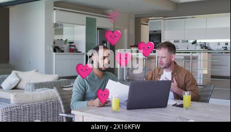 Image of heart icons over diverse gay couple using laptop Stock Photo