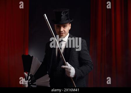 Magician performing miracle trick on stage using fan and cane Stock Photo