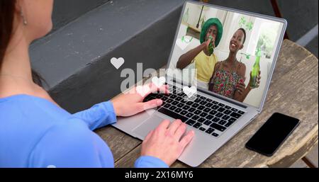 Multiple white heart icons floating over caucasian girl having a imagecall on laptop at a cafe Stock Photo