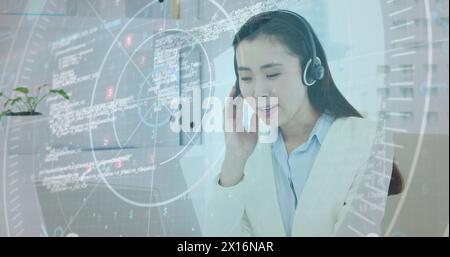 Image of data processing over asian businesswoman wearing phone headset using laptop at office Stock Photo