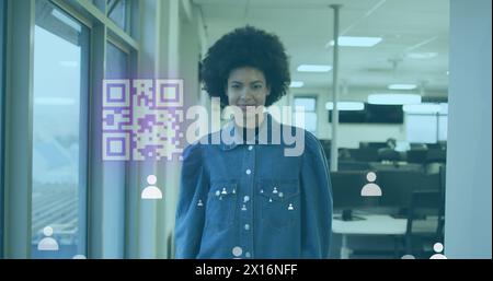 Image of gr code and icons over biracial woman smiling in office Stock Photo