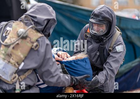 A man in a hazmat suit is helping a woman with a baby. The scene is tense and serious, as the man is wearing a gas mask and the woman is holding a bab Stock Photo