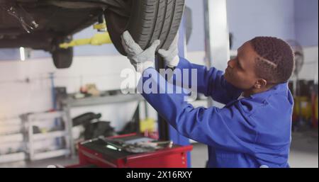 Image of glowing light over african american man working in car workshop Stock Photo