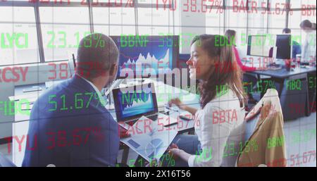 Diverse team analyzing business graphs on laptop in office Stock Photo