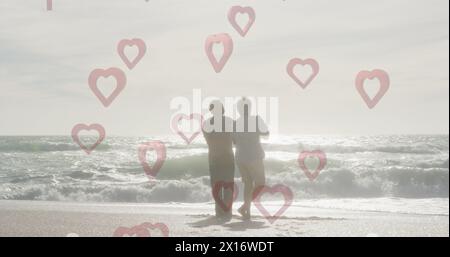 Image of red hearts over couple in love dancing on beach Stock Photo