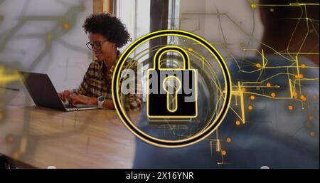 Image of padlock in circle and navigation pattern over smiling biracial woman working on laptop Stock Photo