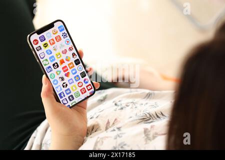 KYIV, UKRAINE - APRIL 1, 2024 Many apps icon on smartphone screen in young female hands indoors. Woman using iPhone app at home Stock Photo