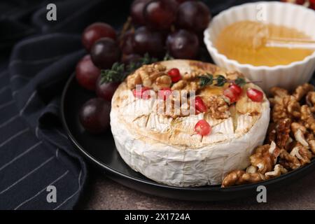 Plate with tasty baked camembert, honey, grapes, walnuts and pomegranate seeds on table, closeup Stock Photo