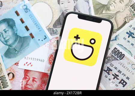 KYIV, UKRAINE - APRIL 1, 2024 Hago icon on smartphone screen on many asian money bills. iPhone display with app logo with japanese yen and chinese yuan banknotes Stock Photo