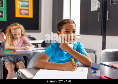 In school, young biracial male student sitting at a desk in a classroom, looking thoughtful Stock Photo