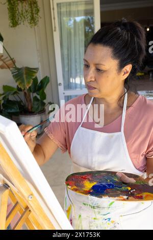 Mature biracial woman painting on canvas at home, focused Stock Photo