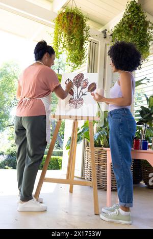 Mature biracial woman and young biracial woman are painting together on porch at home Stock Photo