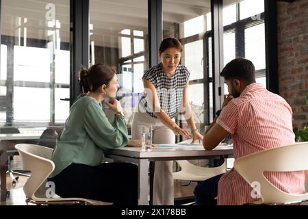 A mature Asian female professional is showing tablet to young colleagues in a modern business office Stock Photo