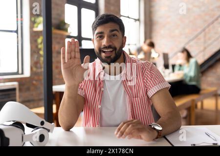 A young Asian male professional wearing striped shirt is waving on video call Stock Photo