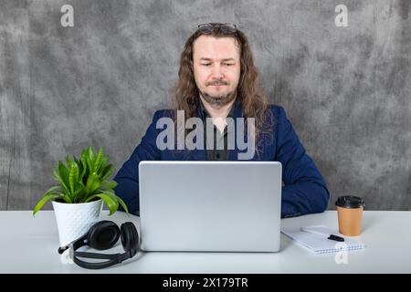 Stylish Long-Haired Man in Blue Suit Posing with Laptop and Headphones Stock Photo