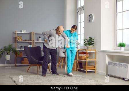 Female medical worker helping senior man to walk with his crutch Stock Photo