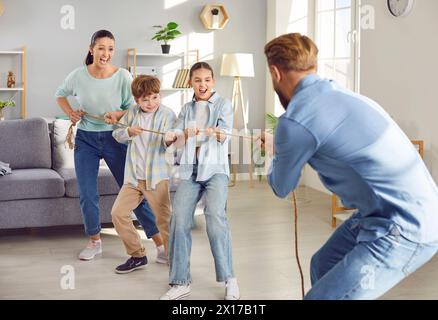Happy joyful smiling children playing together with parents in tug-of-war with a rope at home. Stock Photo