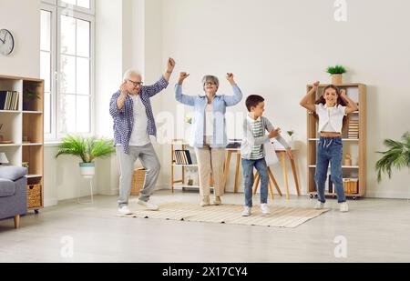 Funny senior couple at home having fun and dancing with their two grandchildren. Stock Photo