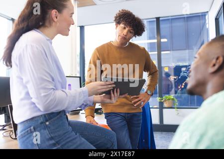 Diverse team discussing over tablet, standing in office Stock Photo