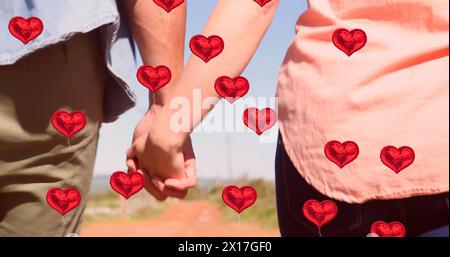 Image of red heart balloons floating over mid section of couple in love holding hands and walking Stock Photo