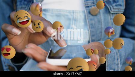 Image of multiple face emojis floating over mid section of a woman using smartphone Stock Photo