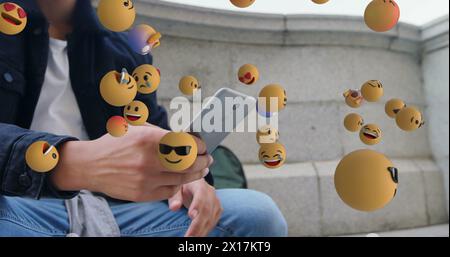 Image of multiple floating emojis over biracial man with curly hair using smartphone Stock Photo