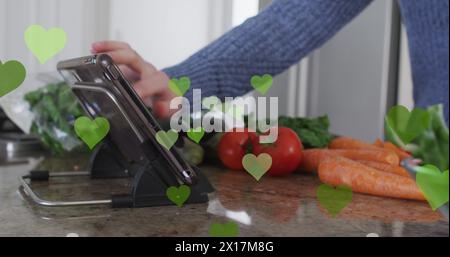 Image of hearts over caucasian man cooking and using tablet Stock Photo