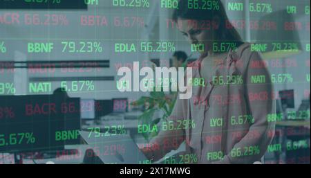 Image of stock market data processing over thoughtful caucasian woman using laptop at office Stock Photo