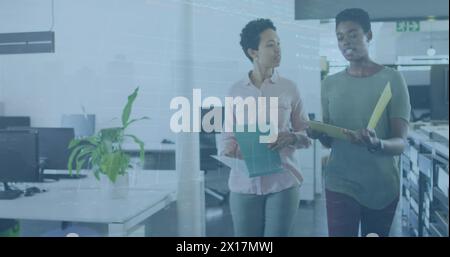 Image of stock market data processing over two diverse women discussing while walking at office Stock Photo