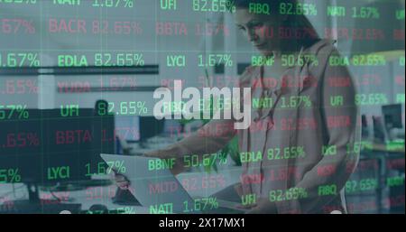 Image of stock market data processing over thoughtful caucasian woman using laptop at office Stock Photo