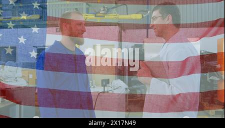 Image of American flag waving over two men working and talking factory in the background Stock Photo