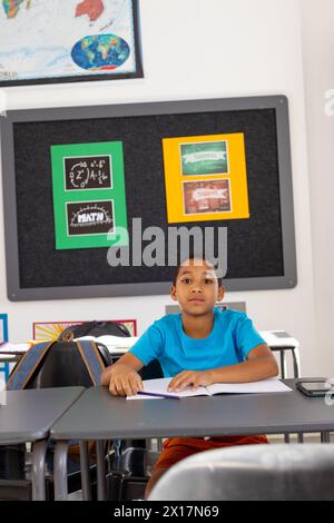 In school, young biracial boy sitting at a desk in a classroom, looking forward Stock Photo